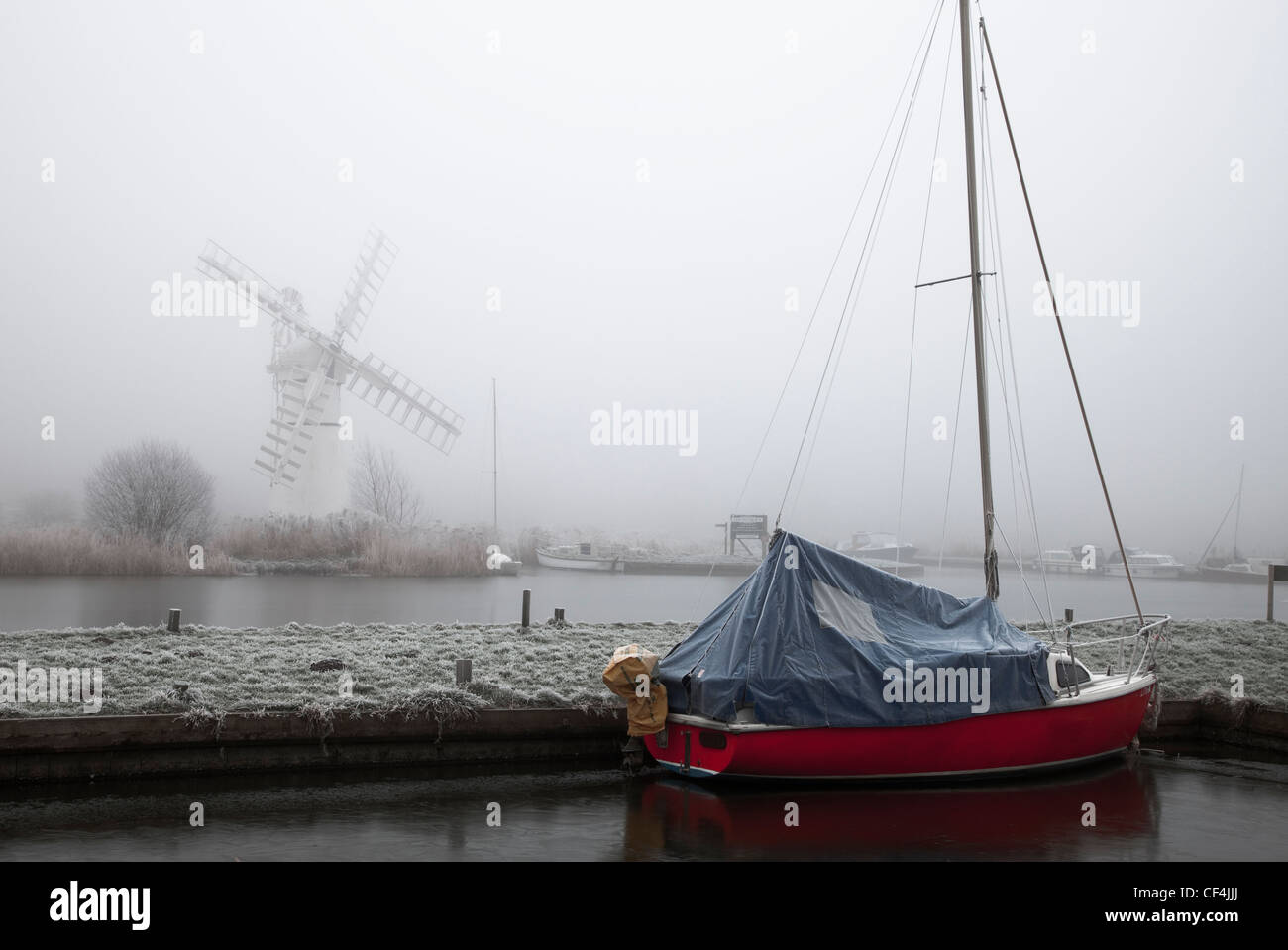 Il mulino a vento di Thurne sorge nella nebbia mentre un rosso barca è ormeggiata in primo piano in Norfolk. Foto Stock