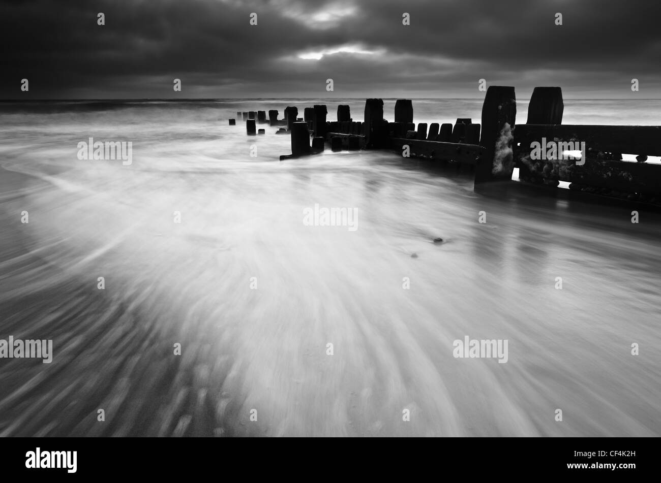 Mare turbinano intorno un groyne in legno come una tempesta raccoglie all'orizzonte. Foto Stock