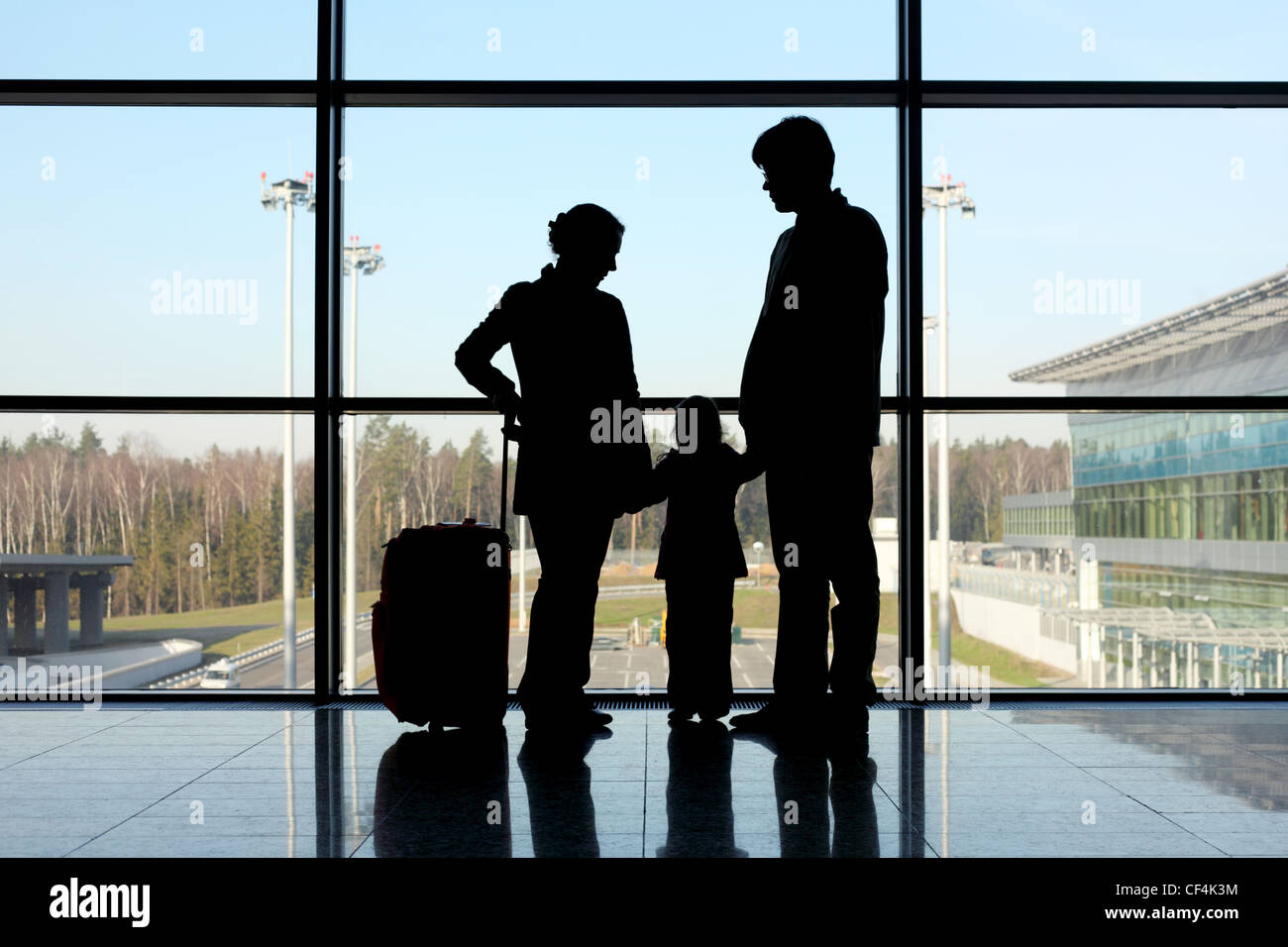 Silhouette della madre, padre e figlia con i bagagli in piedi vicino alla finestra in aeroporto Foto Stock