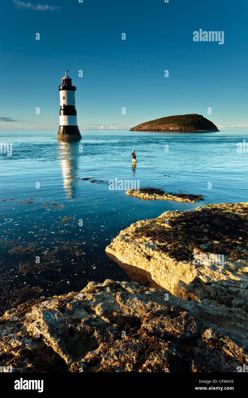 Un uomo pesca nella parte anteriore del faro Penmon e Puffin Island al punto Penmon sull'Isola di Anglesey. Foto Stock