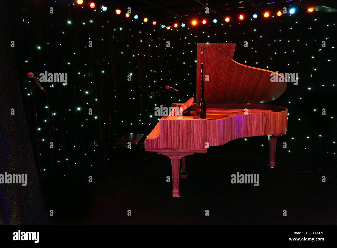 Grand pianoforte presso il palcoscenico di un concerto con la tenda nera decorato lampade multicolori Foto Stock