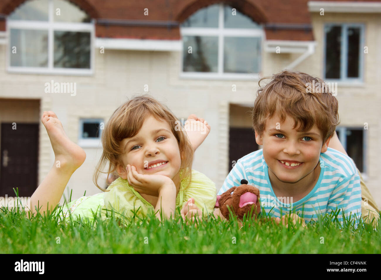 Sorridente fratello e sorella giacente sul prato davanti la casa nuova. Nelle mani del ragazzo giocattolo. Foto Stock