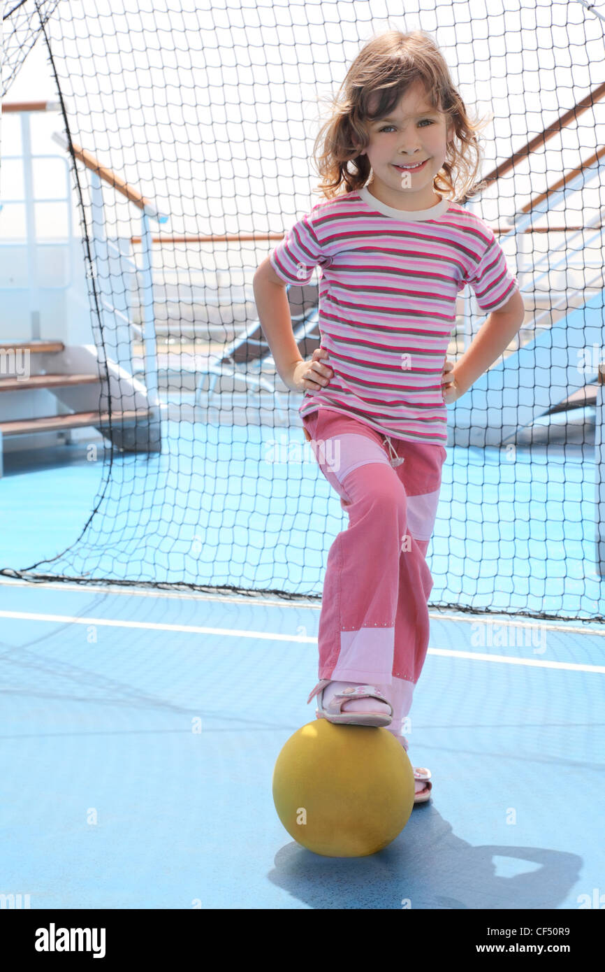 Bambina con sfera gialla in piedi vicino all obiettivo di calcio sulla nave da crociera deck, giorno di estate Foto Stock