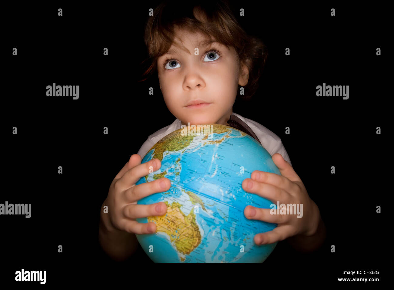 Bambina tiene le mani sul globo del mondo isolati su sfondo nero, Globe è illuminato dall'interno Foto Stock