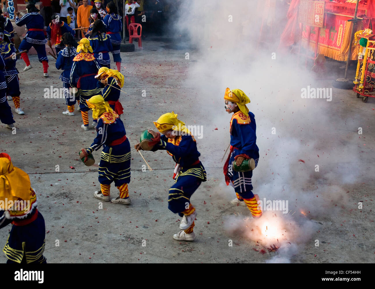 Ragazzi Thai in caratteri cinesi balli in costume e drumming con petardi che esplodono a livello locale tempio Tailandia Bangkok Asia Foto Stock