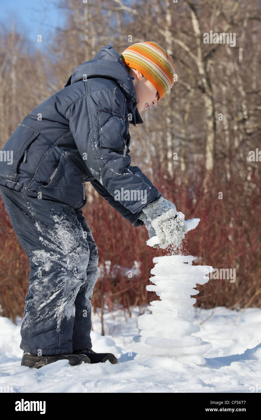 Ragazzo crea piramide dal ghiaccio nella giornata di sole in inverno in legno, equilibrio instabile Foto Stock