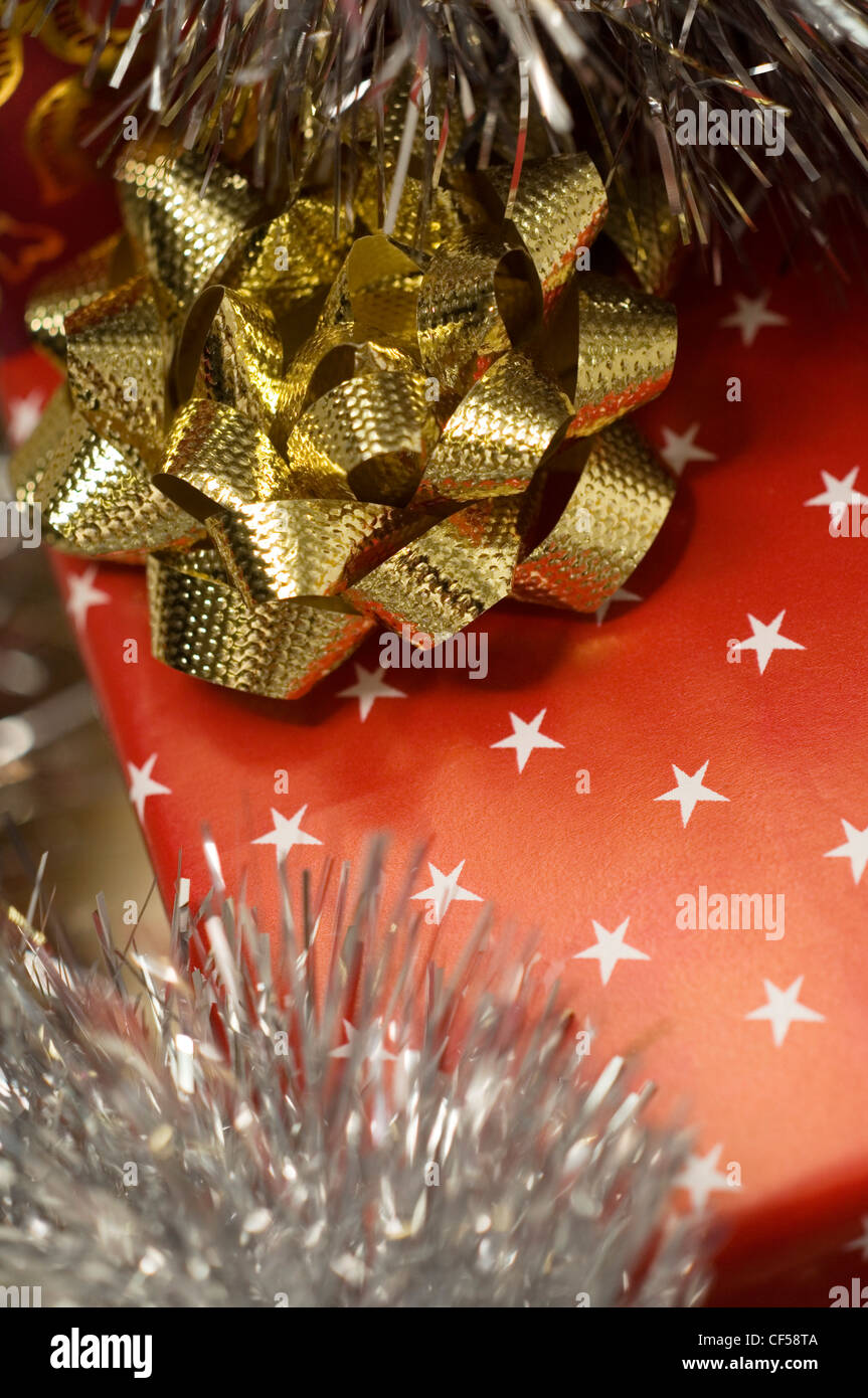 Regalo di natale avvolto con carta di colore rosso con stelle bianche e oro, prua con argento tinsel Foto Stock
