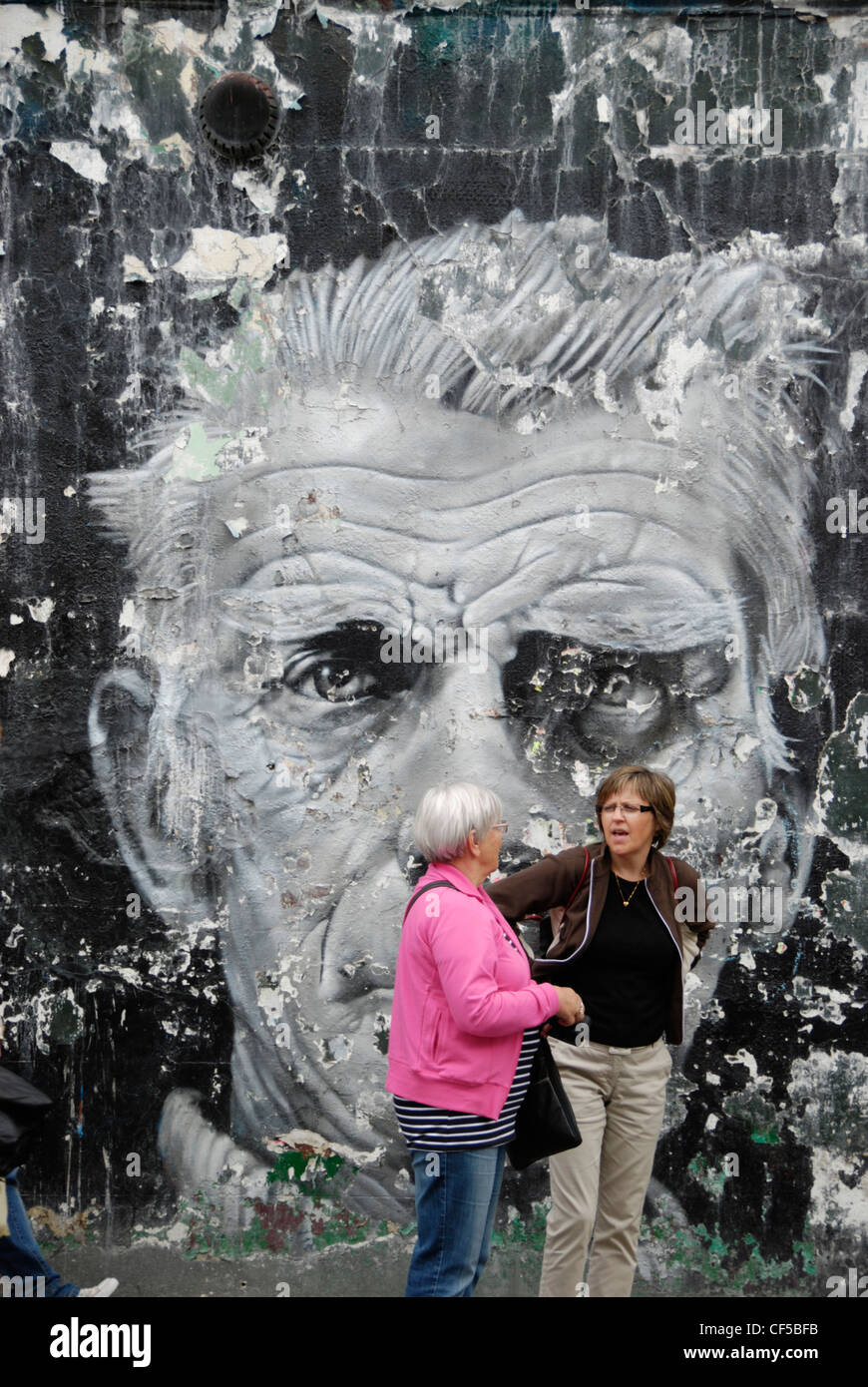 Due turisti in piedi di fronte a un grande murale di Samuel Beckett di Blenheim Crescent vicino a Portobello Road. Foto Stock