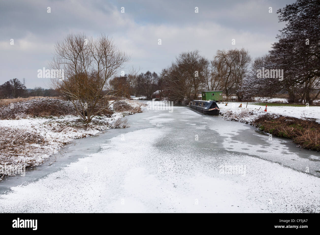 Paesaggio Innevato in Surrey, sul fiume Wey, con neve sulla superficie ghiacciata e longboat chiatta ormeggiata sulla riva del fiume vicino Pyrford Foto Stock