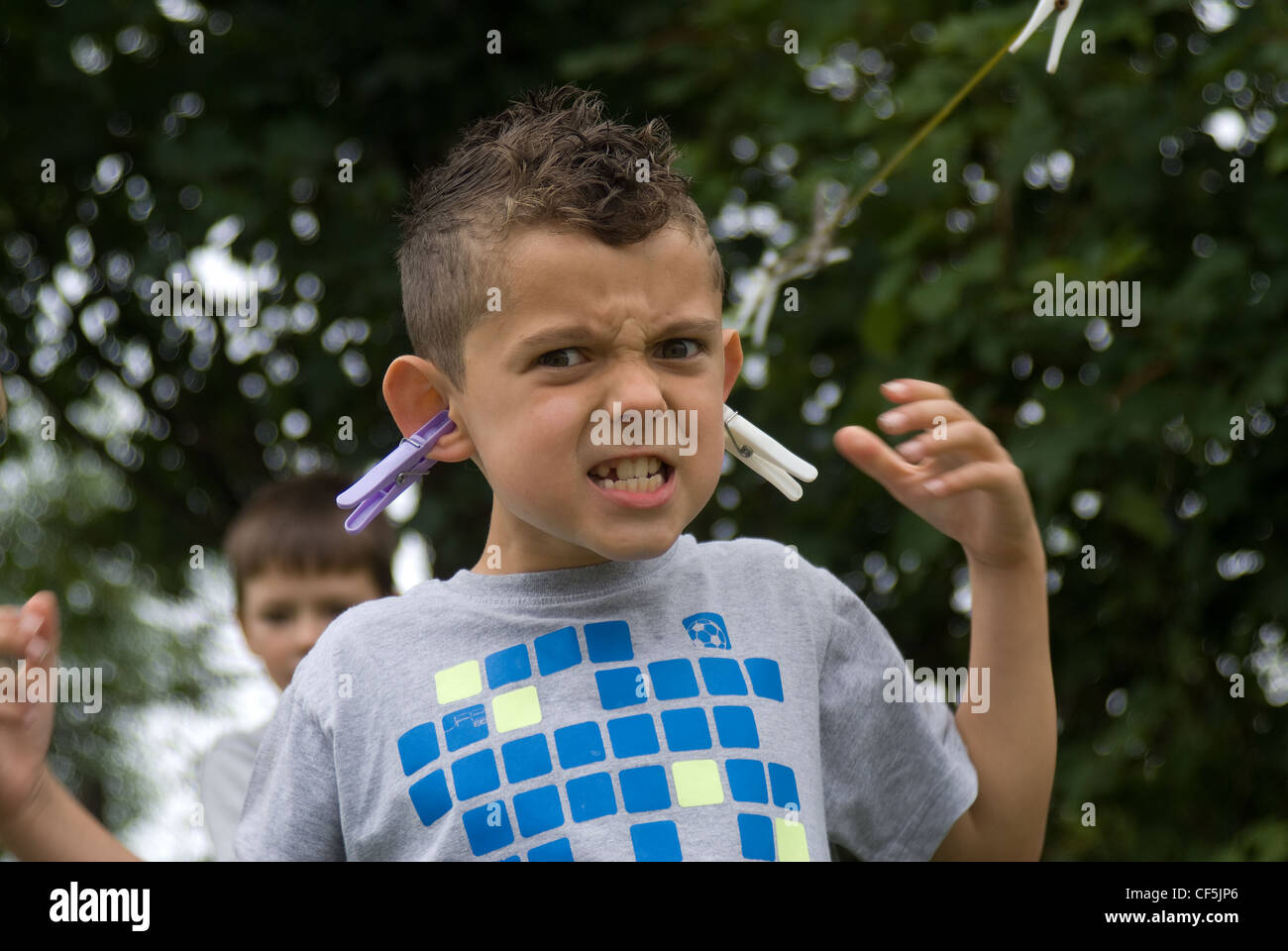 Giovane ragazzo giocando nel cortile clipping mollette sulle sue proprie  orecchie con una grande espressione sfocata la massa posteriore Foto stock  - Alamy