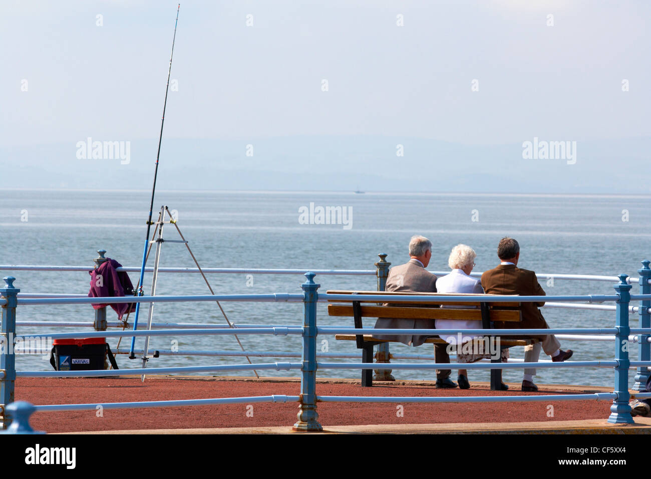 Tre persone seduto alla fine di un molo che guarda al mare a Morecambe. Foto Stock