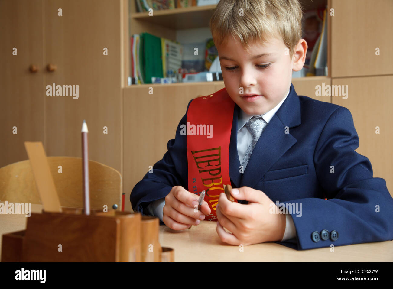 Di prima classe. Ragazzo in uniforme scolastica alla sua scrivania, la penna in mano. Foto Stock