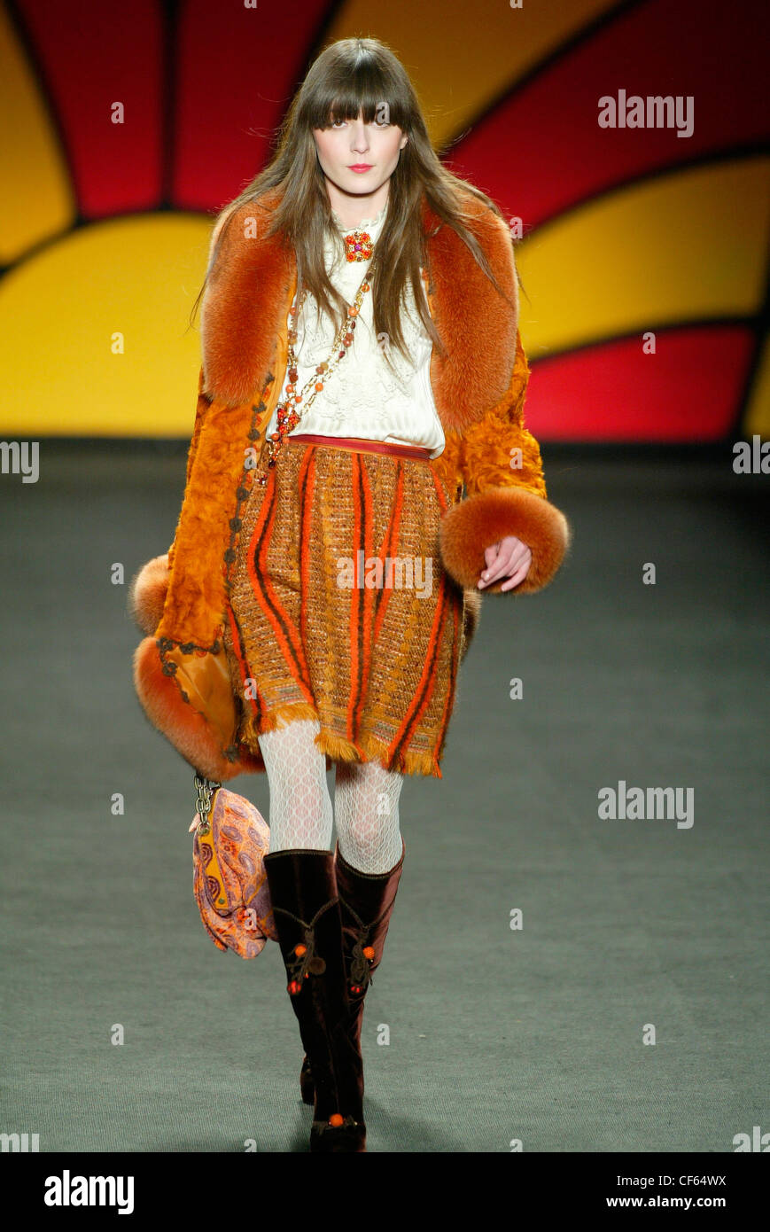 Bruna modello femminile capelli lunghi e spessi fringe indossando una schiacciata di velluto cappotto arancione arancione fur trime su un color crema Foto Stock