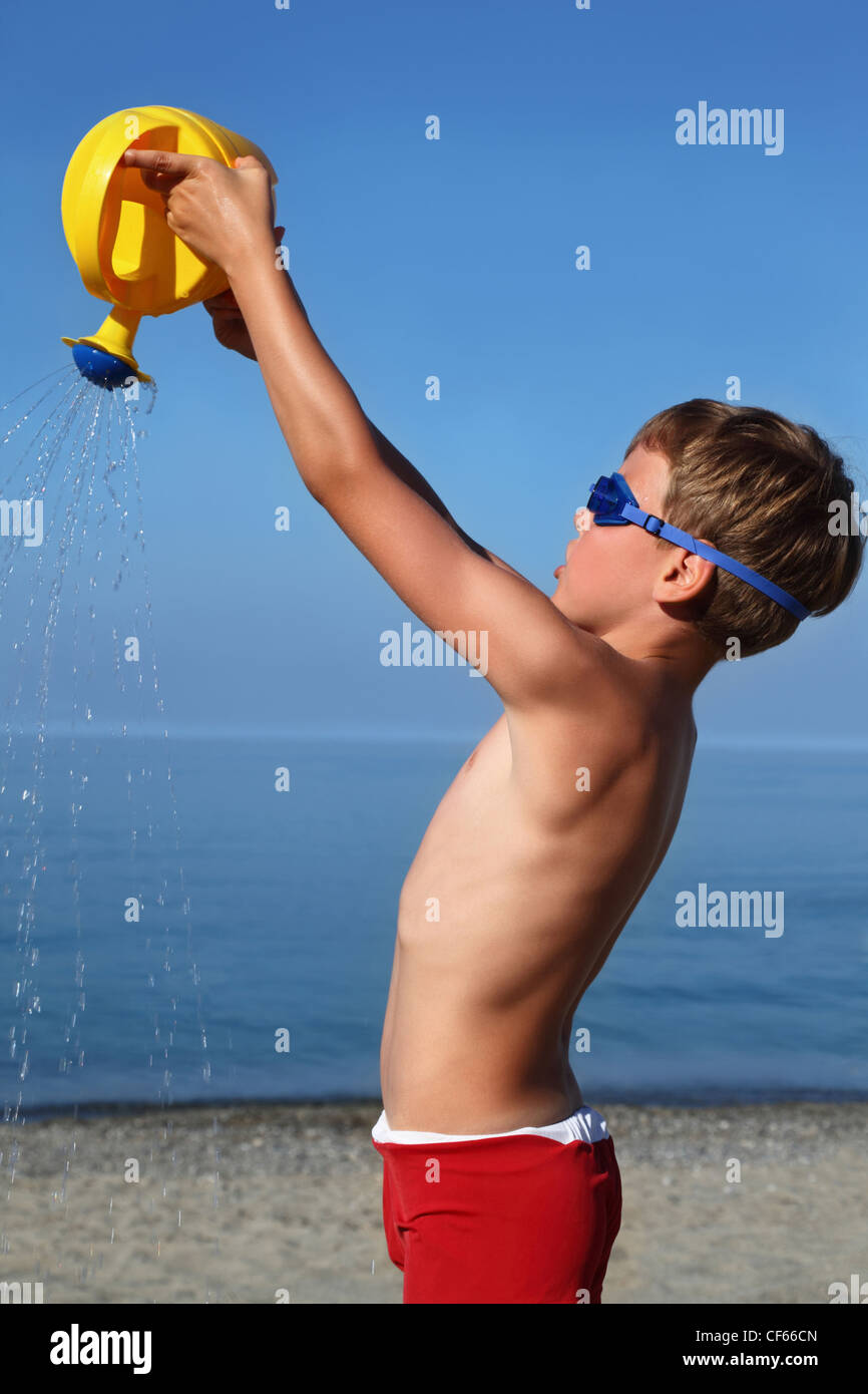 Ragazzo sorge sulla spiaggia in un giorno di tempo e si versa la sabbia di innaffiatoio mano di sollevamento Foto Stock