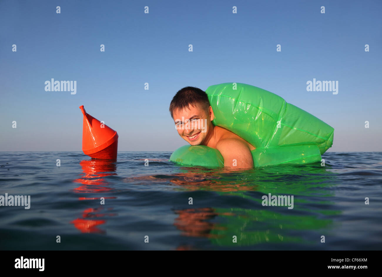 Giovane uomo nuota in mare sul verde lifeline. arancione boa di ancoraggio galleggia sul mare. Foto Stock