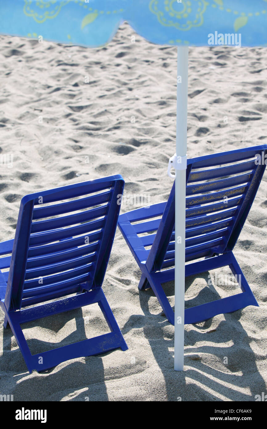 Due blu scuro sedie in plastica stare sulla spiaggia sotto ombrellone Foto Stock