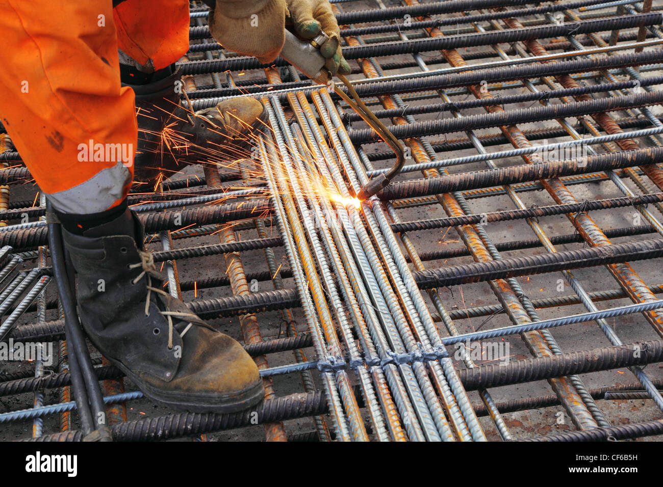 Gambe del lavoratore in vestiti arancioni saldare reticolo metallico dalla torcia di acetilene Foto Stock