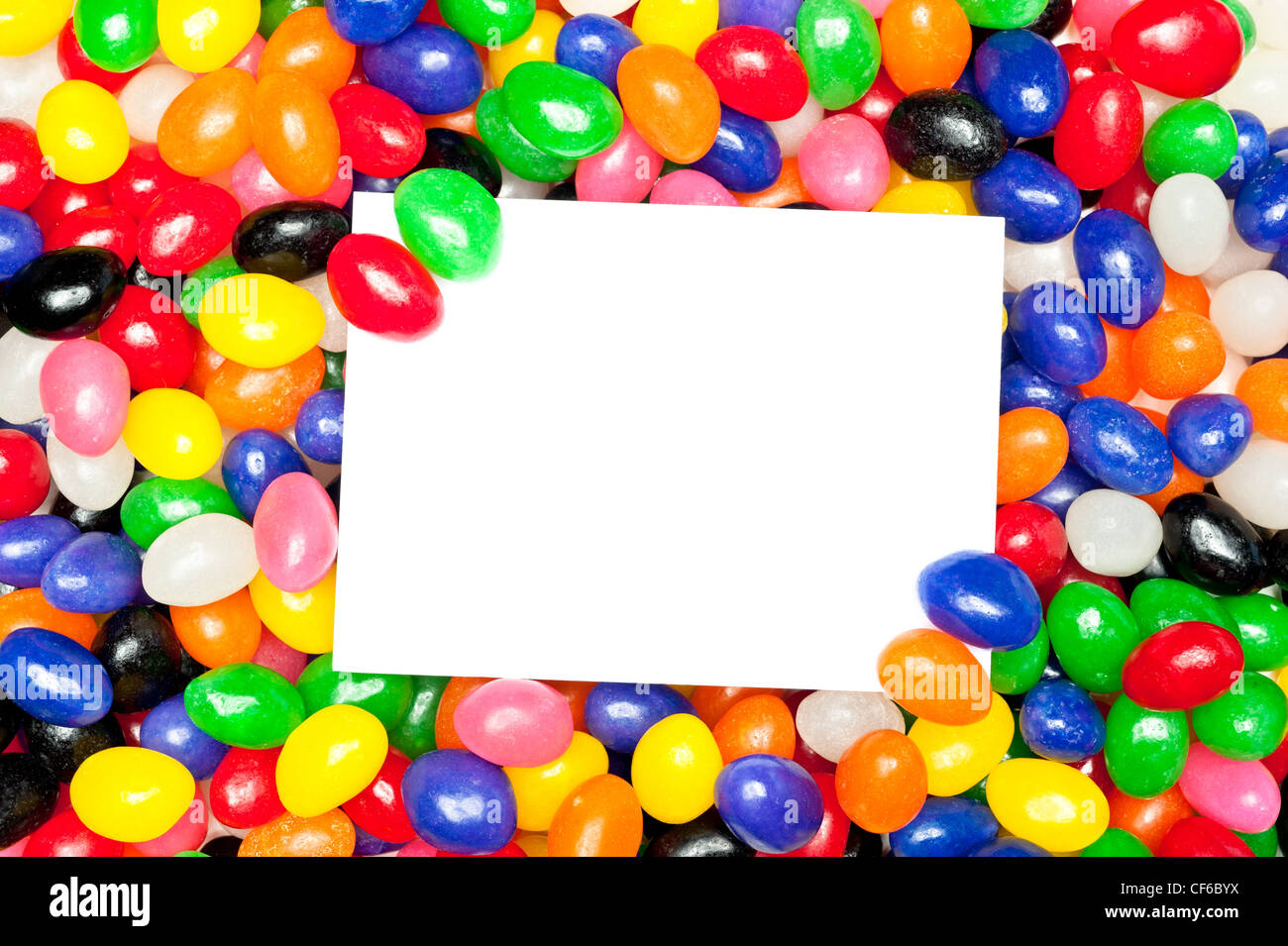 Un messaggio vuoto card in un mucchio di jellybeans colorati. I progettisti possono utilizzare carta per posizionare la copia. Foto Stock
