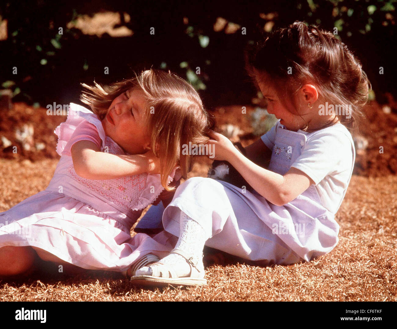 Due bambini di sesso femminile combattimenti profilo del bambino femmina brunette capelli indossando t shirt sotto pinafore abito bianco calzini e Foto Stock