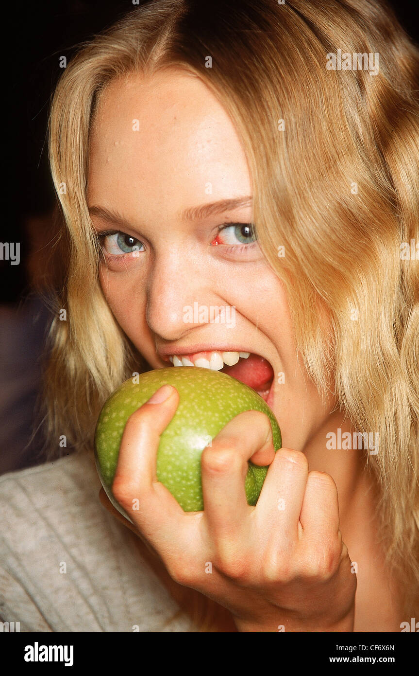 Backstage Milano Primavera Estate Burberry modello Gemma Ward ondulata lunghi capelli biondi che indossa un coperchio grigio mordere nella grande mela verde, Foto Stock
