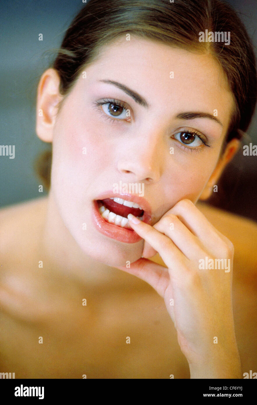 Femmina bruna cercando di fotocamera, toccare la sua parte anteriore dei denti inferiori con il suo dito mignolo Foto Stock
