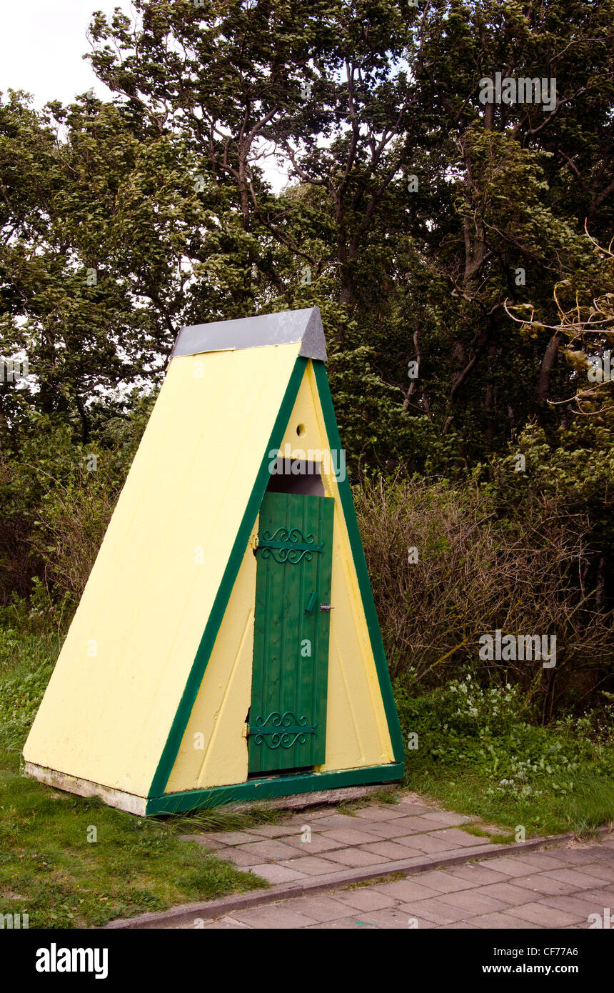 Esterno decorativo wc wc vicino al parco di alberi. Giallo parete in mattoni con verde porta di legno. Foto Stock