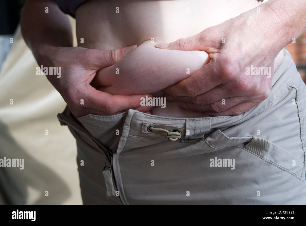 Close up della donna nella sua 40s sollevando la sua parte superiore e spremendo il suo pancino. Donna preoccupati per il suo peso. La perdita di peso. Dieta. Foto Stock