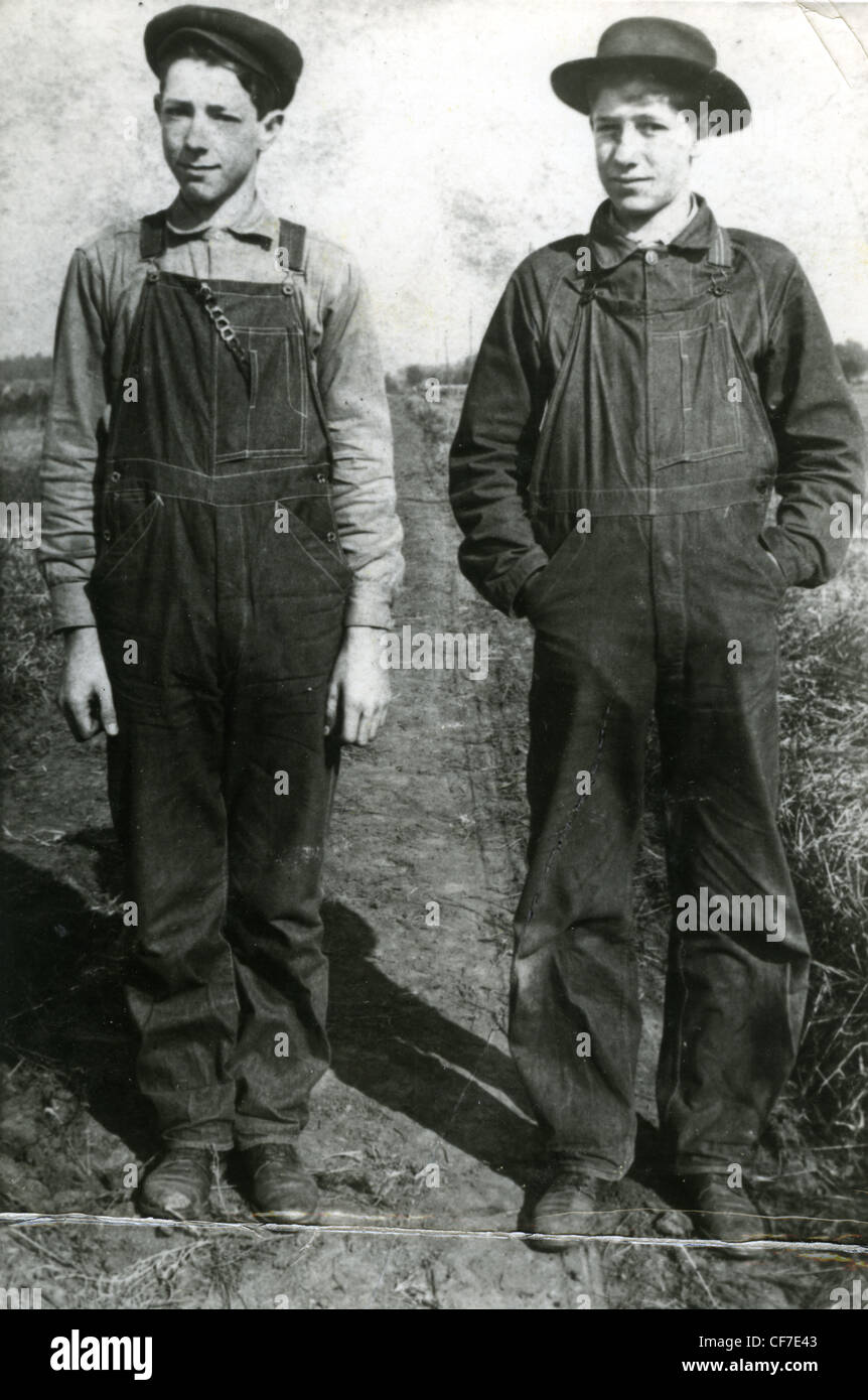 Fattoria di due ragazzi in tuta di stand per un ritratto in un campo durante gli anni venti o trenta grande depressione agricoltura la moda maschile di brodo Foto Stock