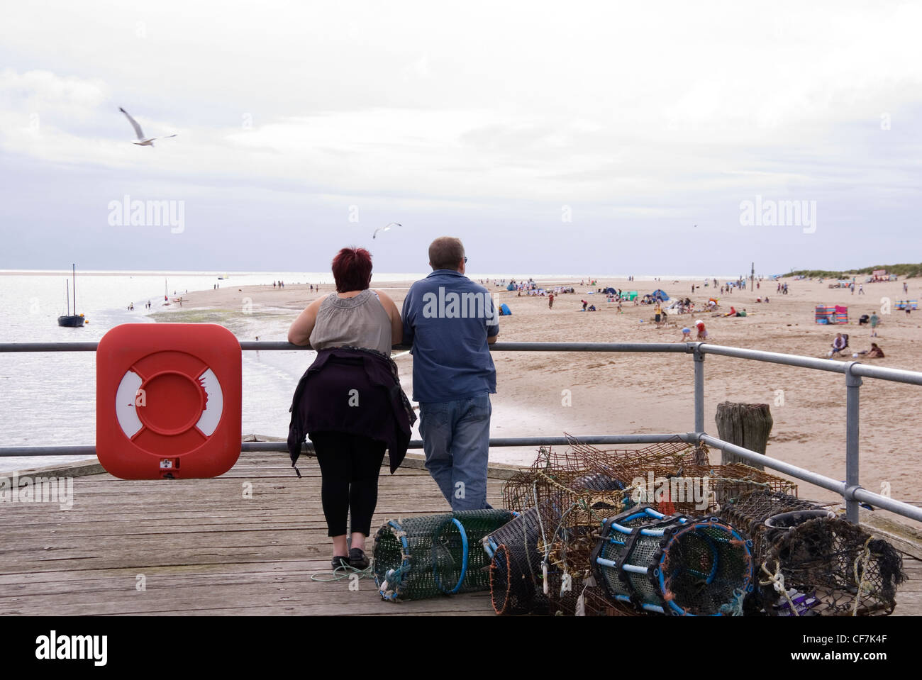 Giovane rilassante alla fine del molo, guardando le famiglie durante la riproduzione su vasta spiaggia sabbiosa di seguito, Aberdovey, Wales, Regno Unito Foto Stock