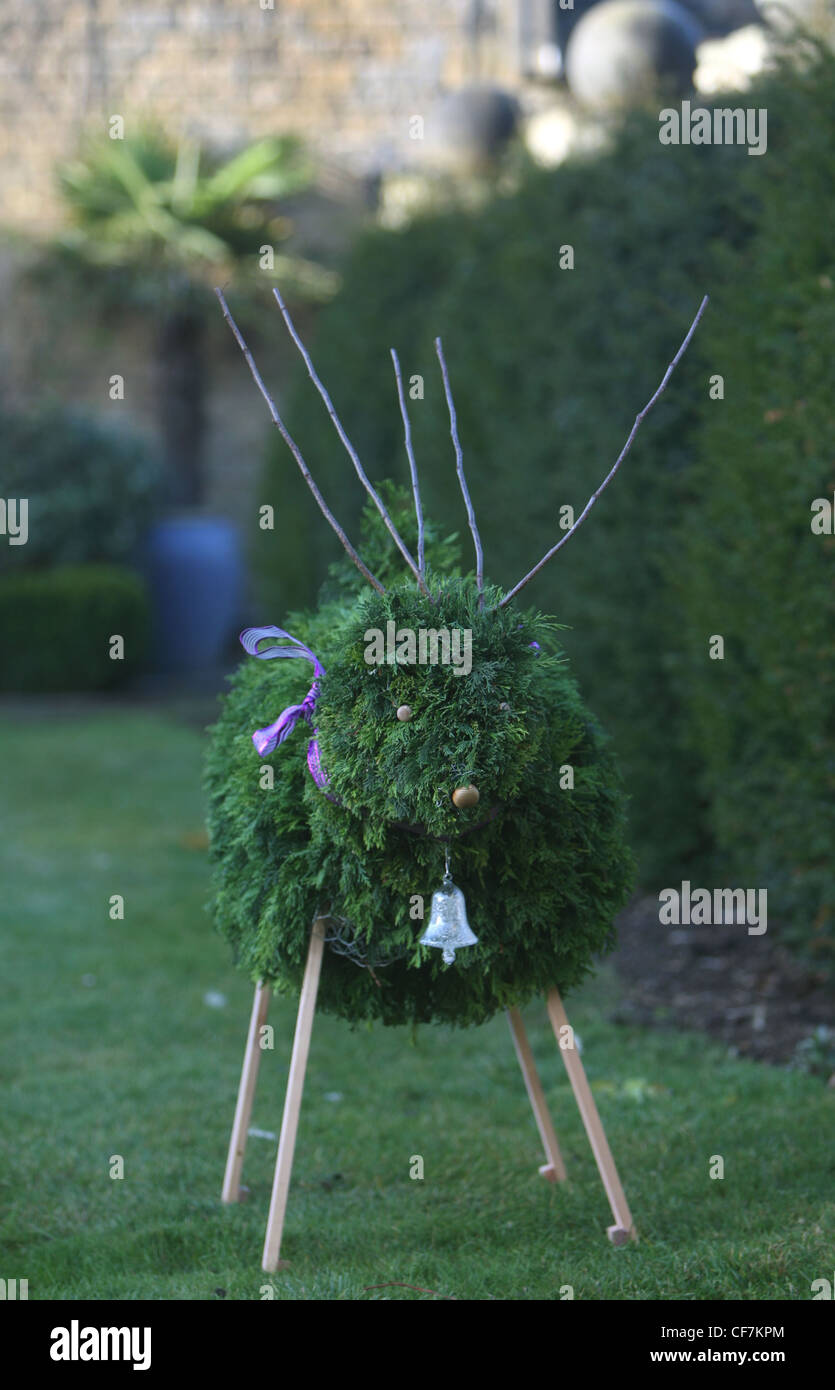 Bunny Guinness rende le decorazioni di Natale animale fatto da rami di albero nastro viola e argento campana, in piedi sul prato verde Foto Stock