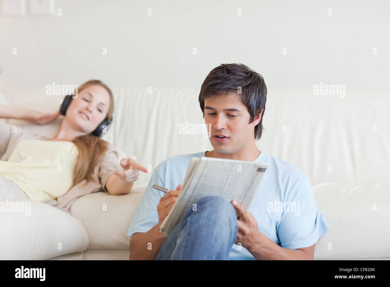 Donna aiutando il suo fidanzato a fare le parole crociate mentre si ascolta la musica Foto Stock
