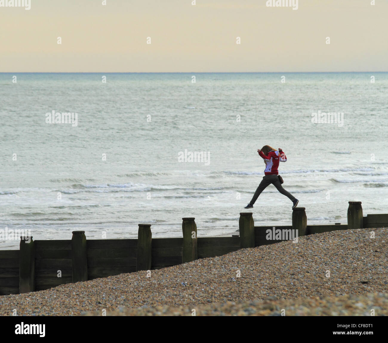 Una giovane ragazza adolescente salti tra i pennelli inguine sulla spiaggia a Eastbourne, East Sussex, Inghilterra. Foto Stock
