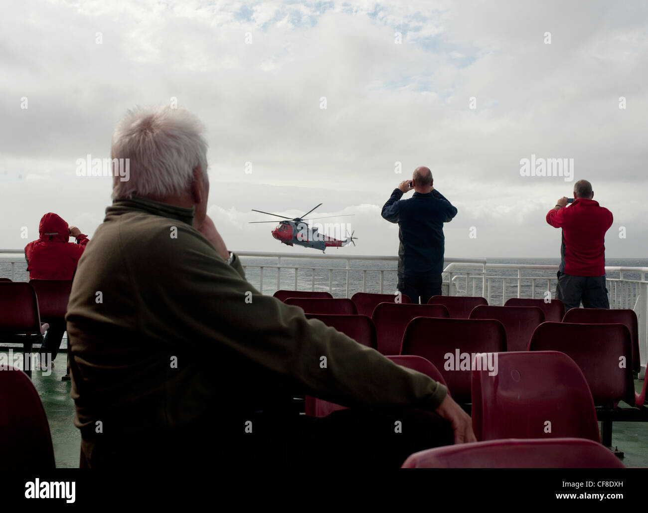Un mare di RAF re elicottero vola sopra il mare come i passeggeri del traghetto a guardare e scattare fotografie dalla barca in Scozia. Foto Stock