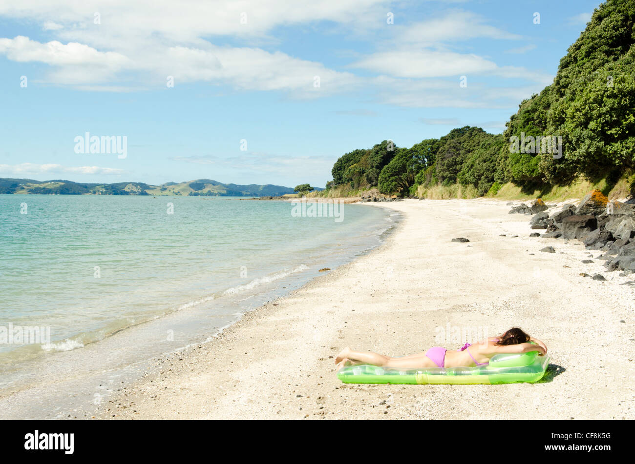 Una donna a prendere il sole su una verde lilo su di una spiaggia appartata in Nuova Zelanda. Foto Stock