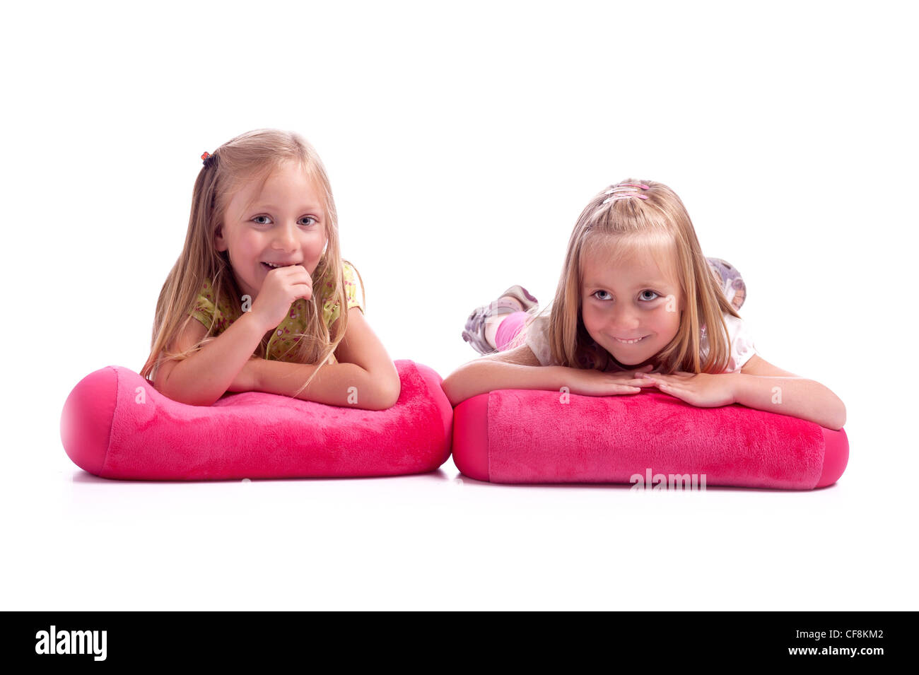 Due bambine che giace un cuscini rosa avendo divertimento. isolato su sfondo bianco Foto Stock