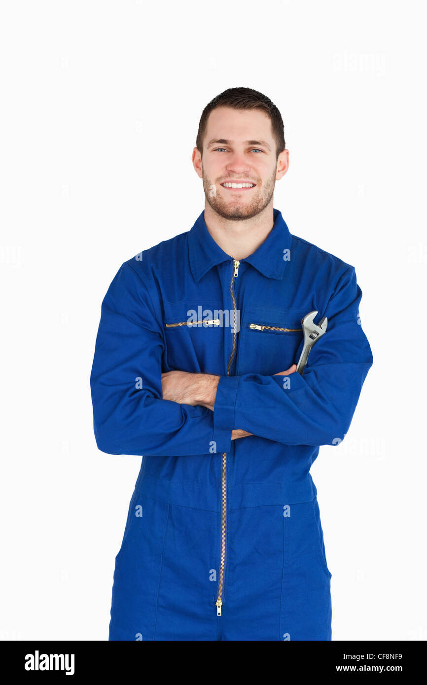Sorridente giovanissimo meccanico nella caldaia tuta con chiave e le braccia incrociate Foto Stock
