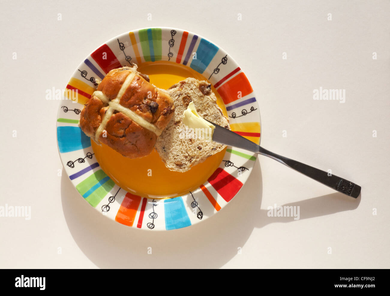 Buttering hot cross bun sulla piastra colorato pronto per Pasqua isolato su sfondo bianco Foto Stock