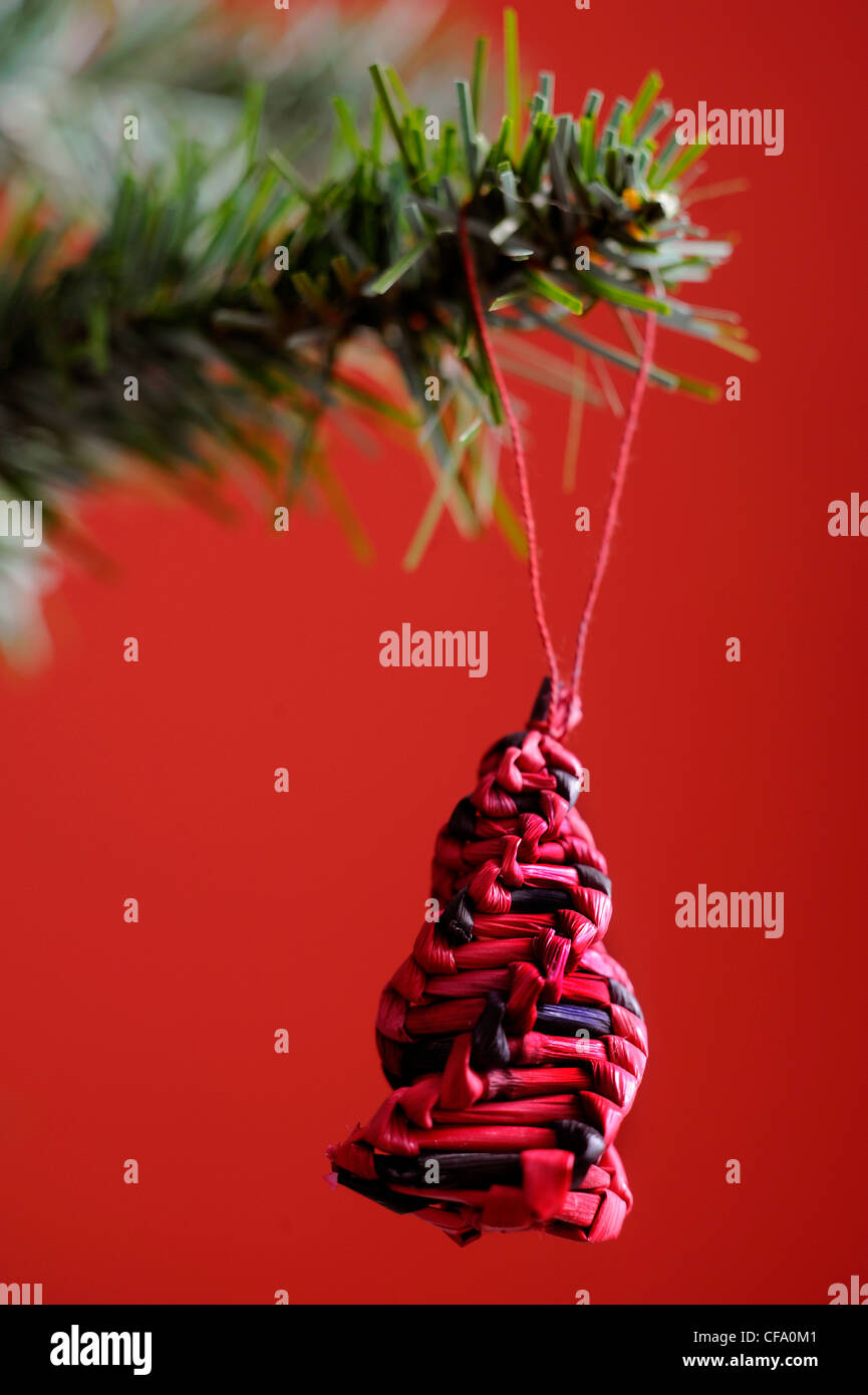 Un nero e rosso il natale a forma di spirale struttura tessuta decorazioni hanging off il ramo di un albero di natale, uno sfondo rosso Foto Stock