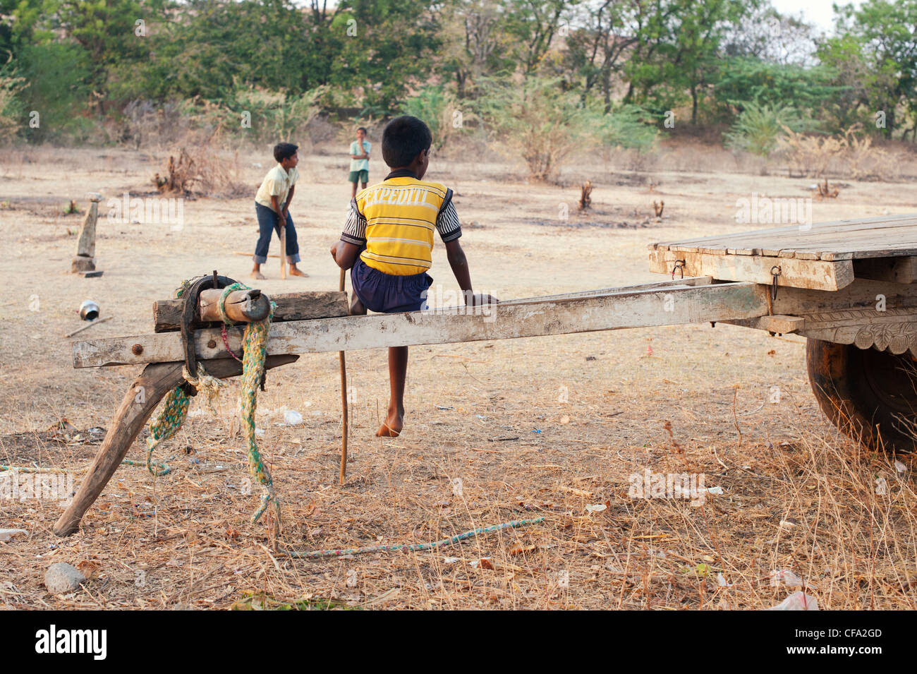 Ragazzo indiano a guardare gli amici a giocare a cricket in secco campagna indiana. Andhra Pradesh, India Foto Stock