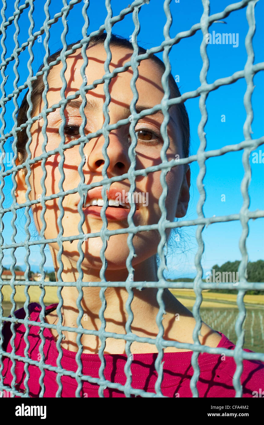 Donna in piedi dietro il recinto metallico con la sua faccia contro la maglia di filo Foto Stock