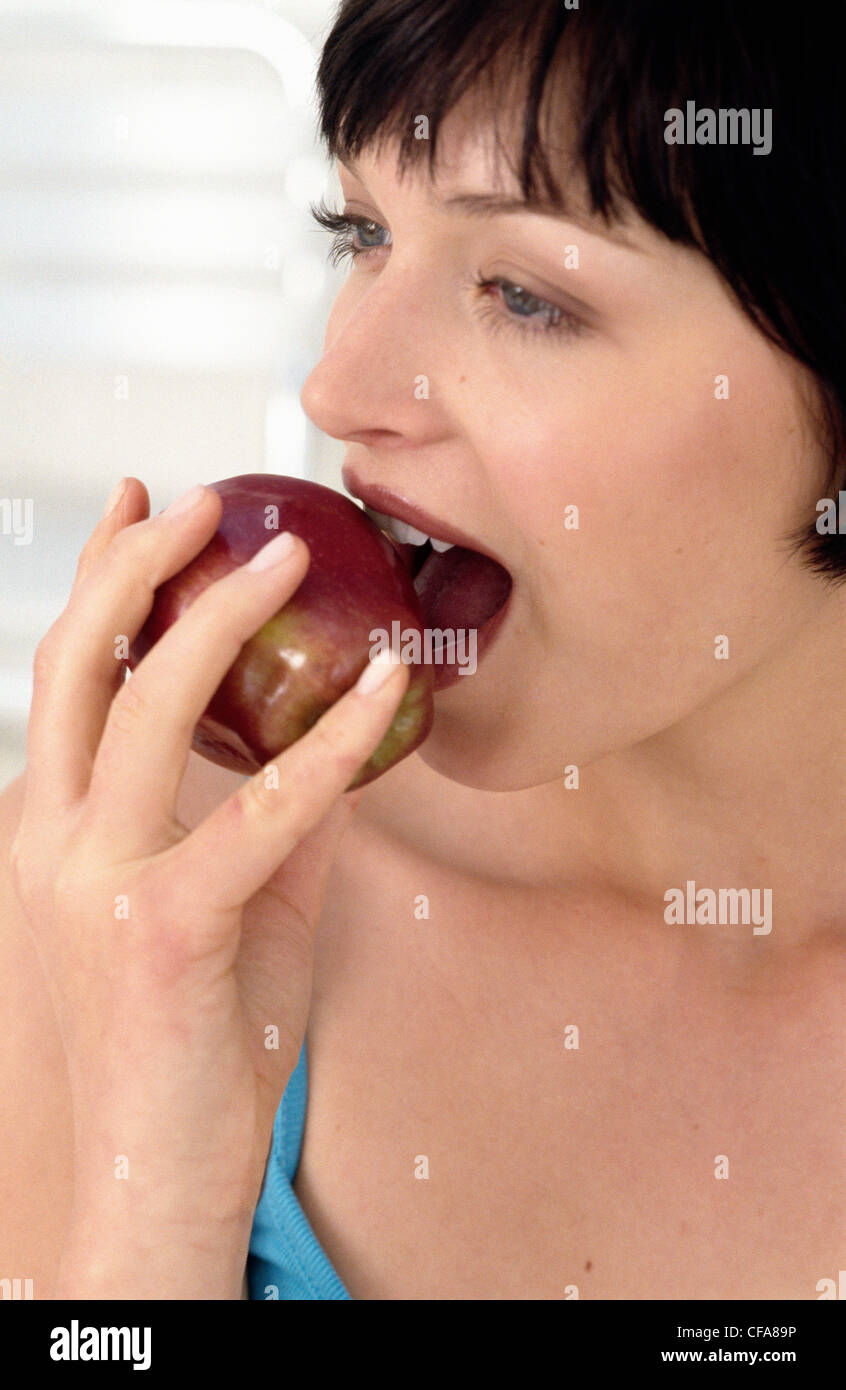 Una donna che guarda a sinistra di mordere in un rosso apple Foto Stock