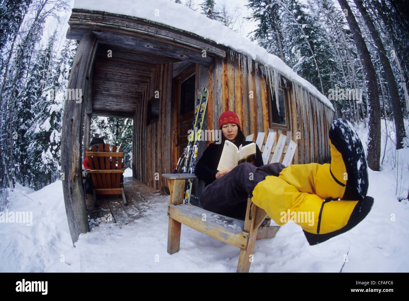 Una giovane donna la lettura di un libro davanti una cabina remoto, gamma Blaeberries, Golden, British Columbia, Canada. Foto Stock