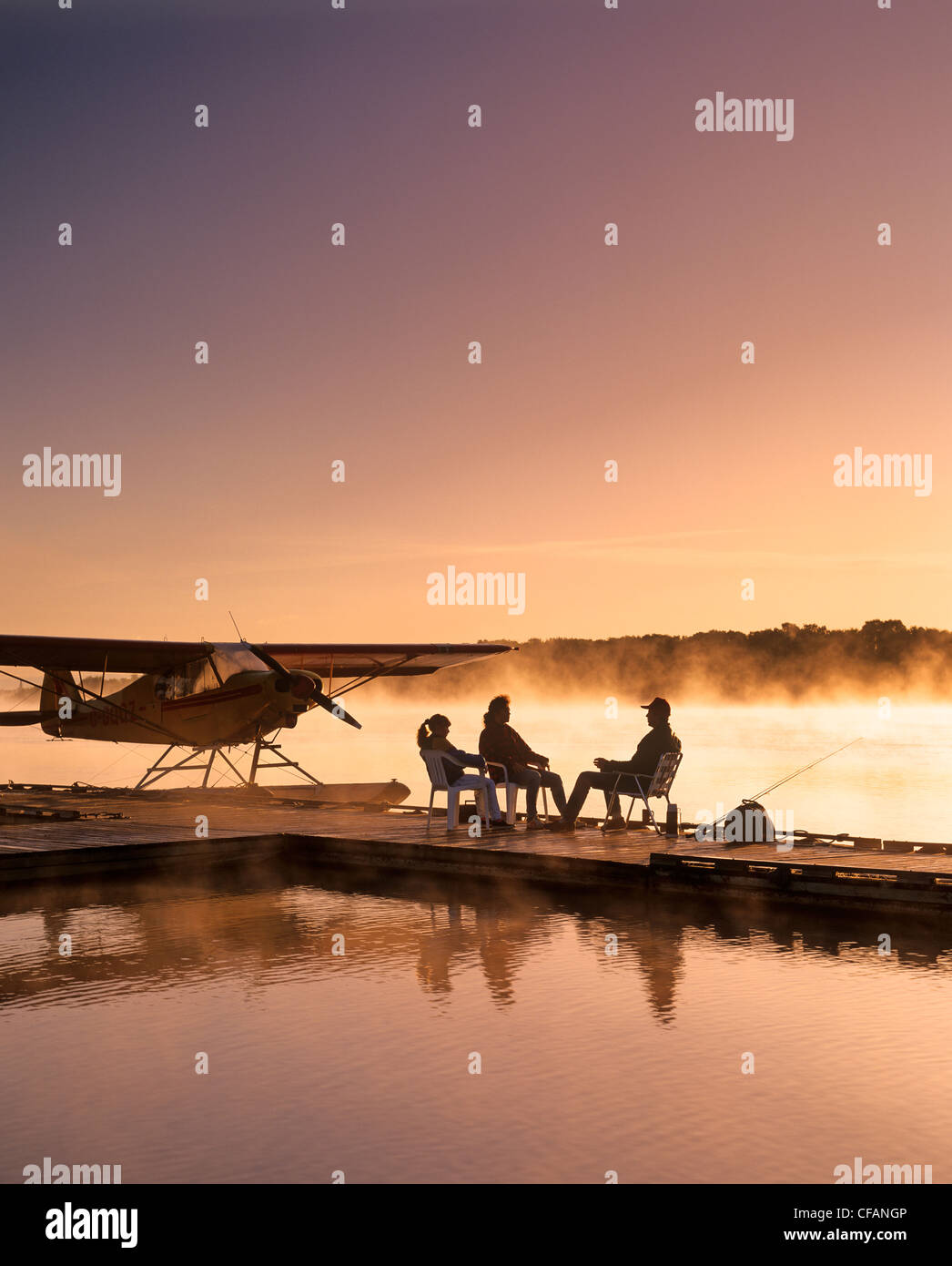 Silhouette di famiglia seduta sul piano galleggiante dock al mattino, Red River, Manitoba, Canada Foto Stock