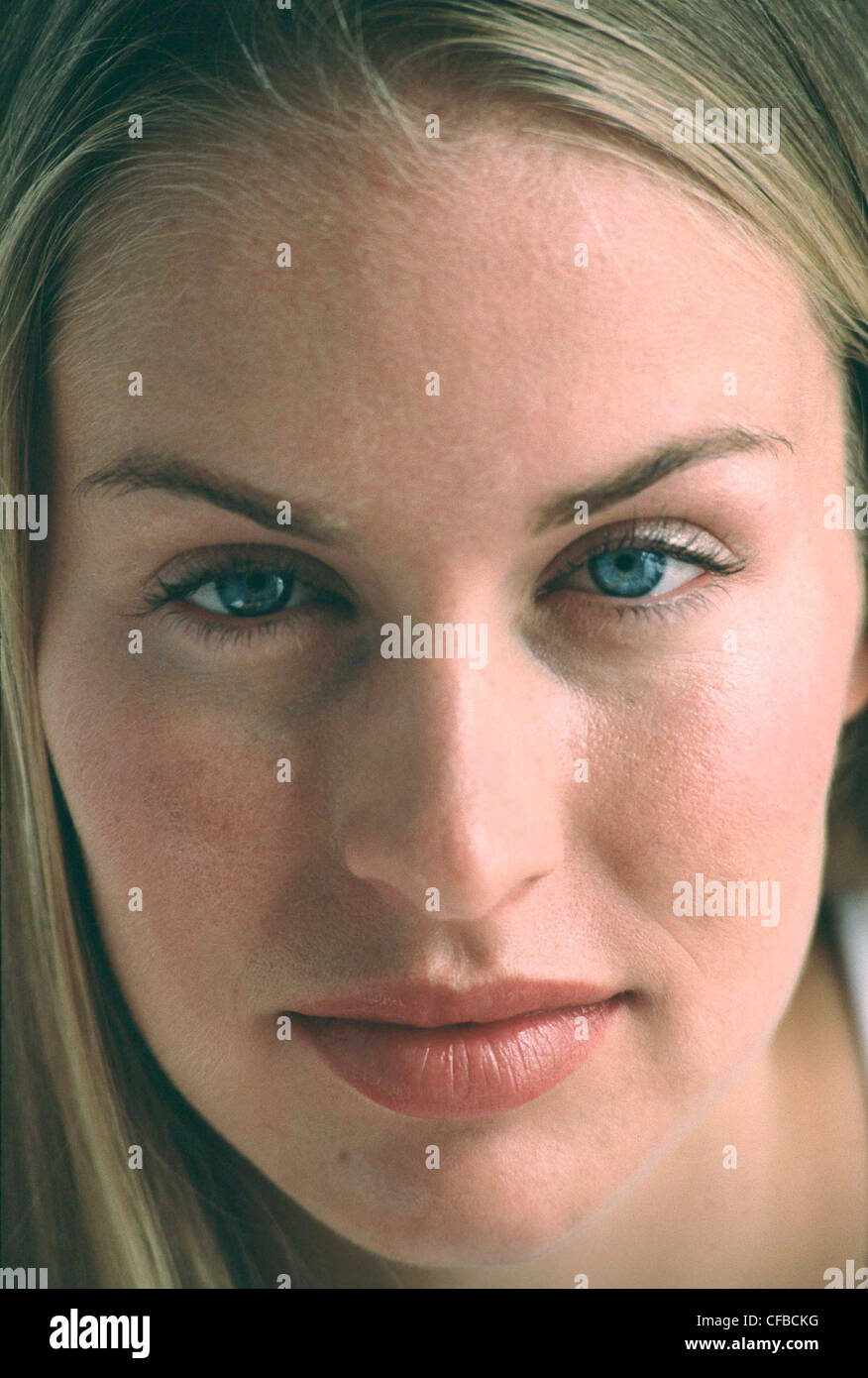 Femmina con lunghi capelli biondi indossa bianco Gilet top sottili compongono cercando di fotocamera con mezzo sorriso Foto Stock