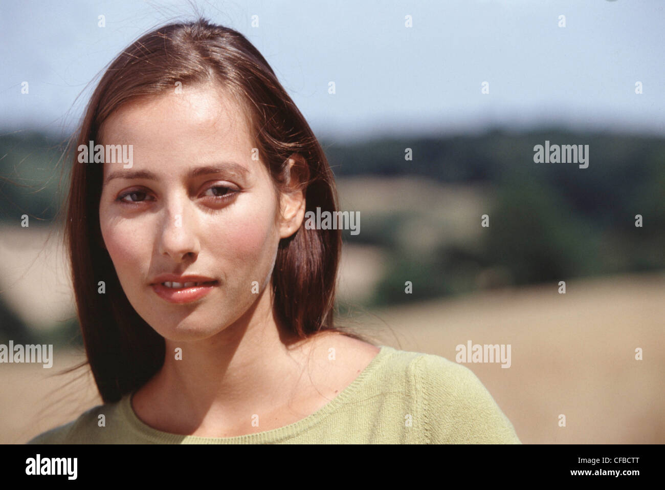 Femmina con lunghi capelli bruna indossa sottili compongono e verde in alto cercando di fotocamera con mezzo sorriso Foto Stock