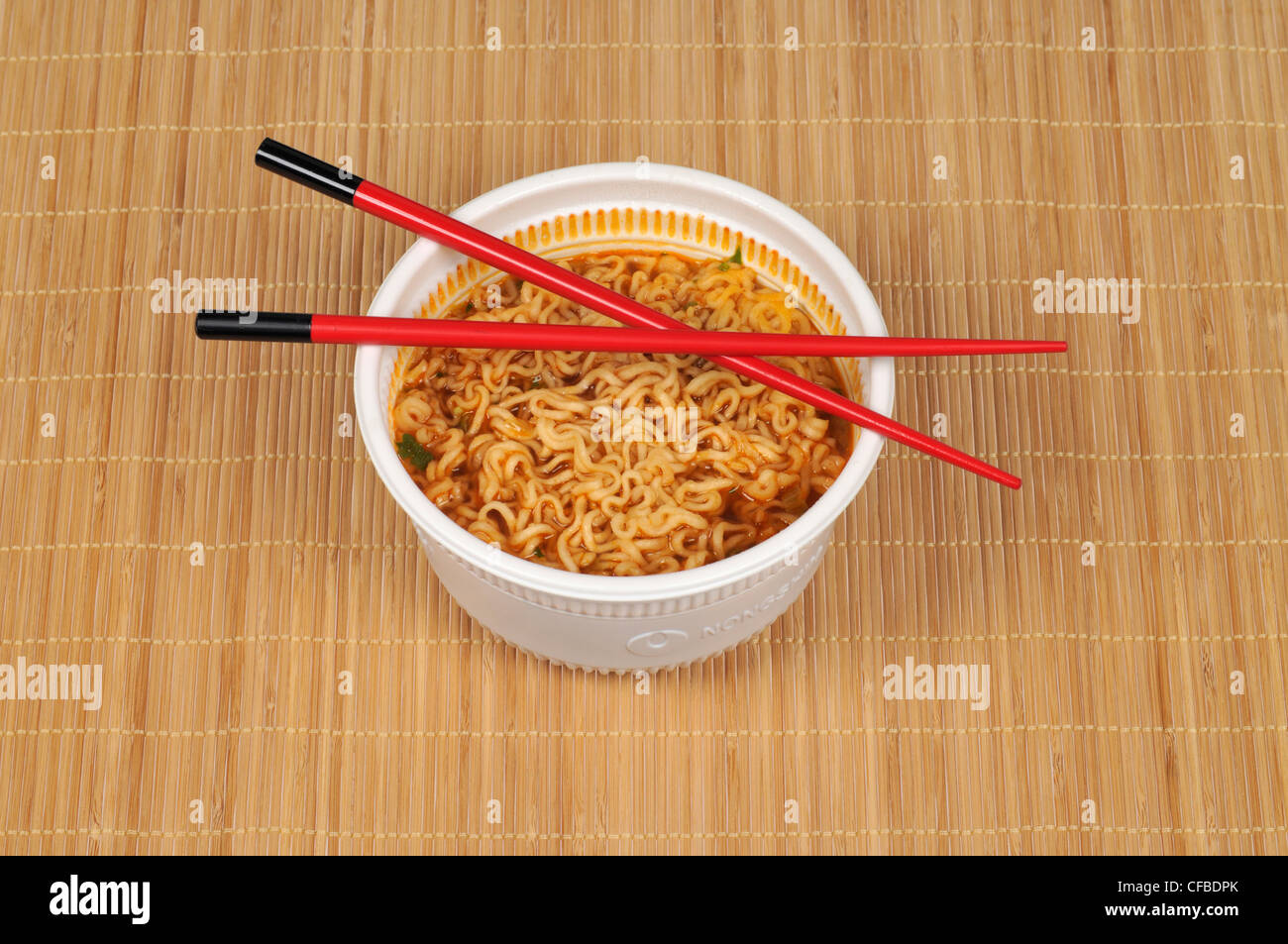 Ciotola di spaghetti orientali con bacchette sul tappetino di bambù Foto Stock