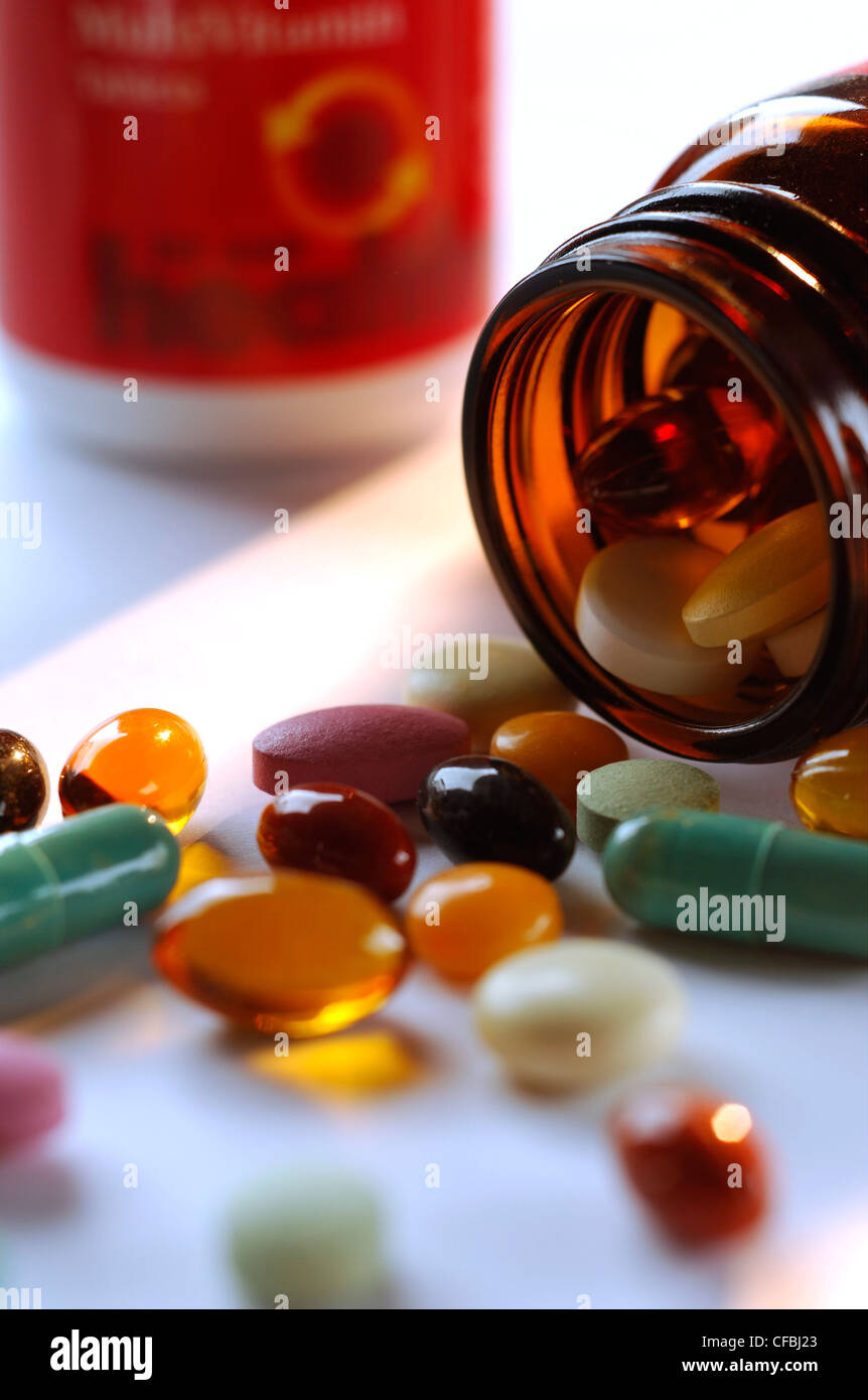 In prossimità di una bottiglia aperta di miste di pillole e capsule su un suo lato con contenuti fuoriuscita e un contenitore in background Foto Stock