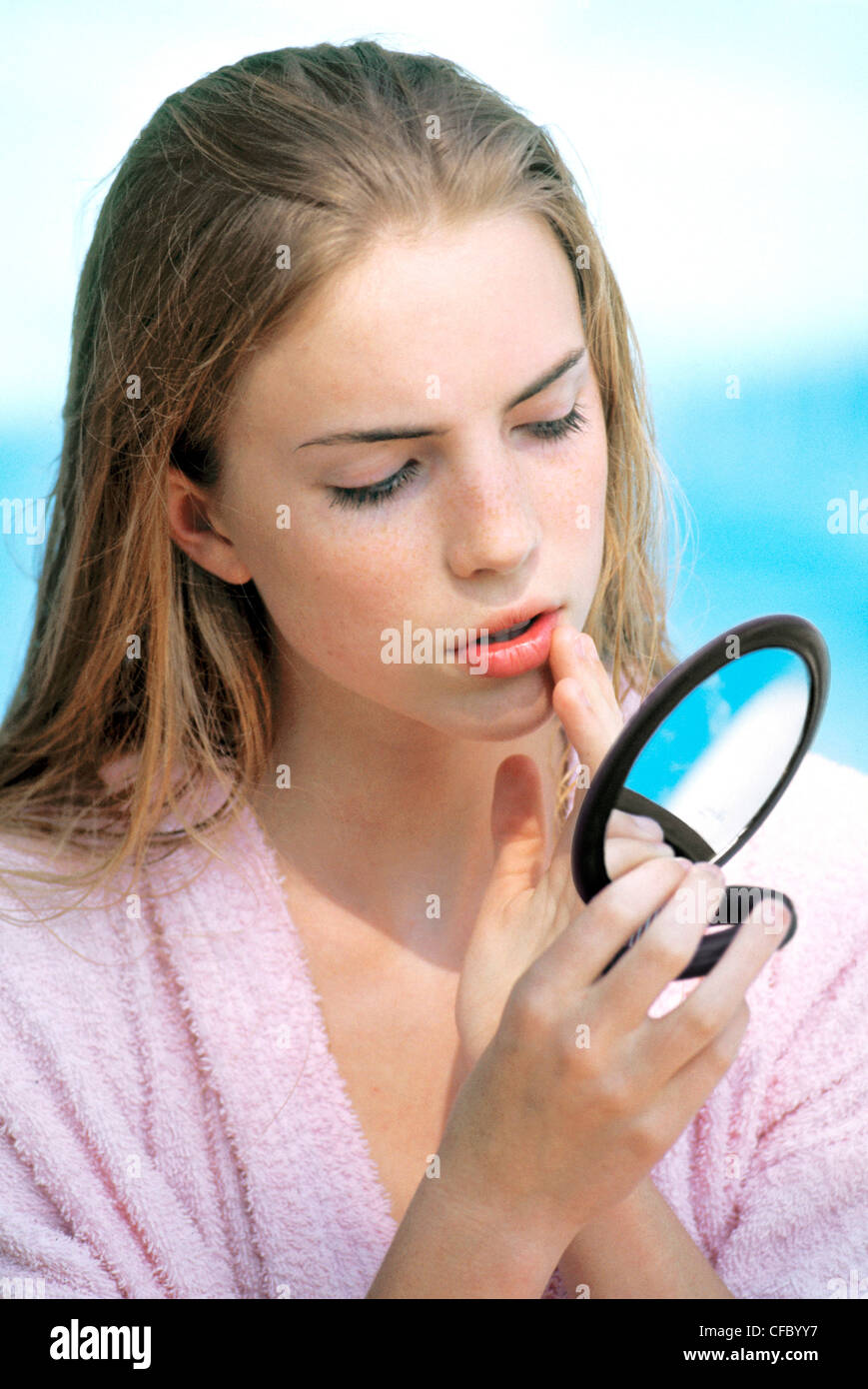 Femmina tenendo un piccolo specchio toccando il suo labbro Foto Stock