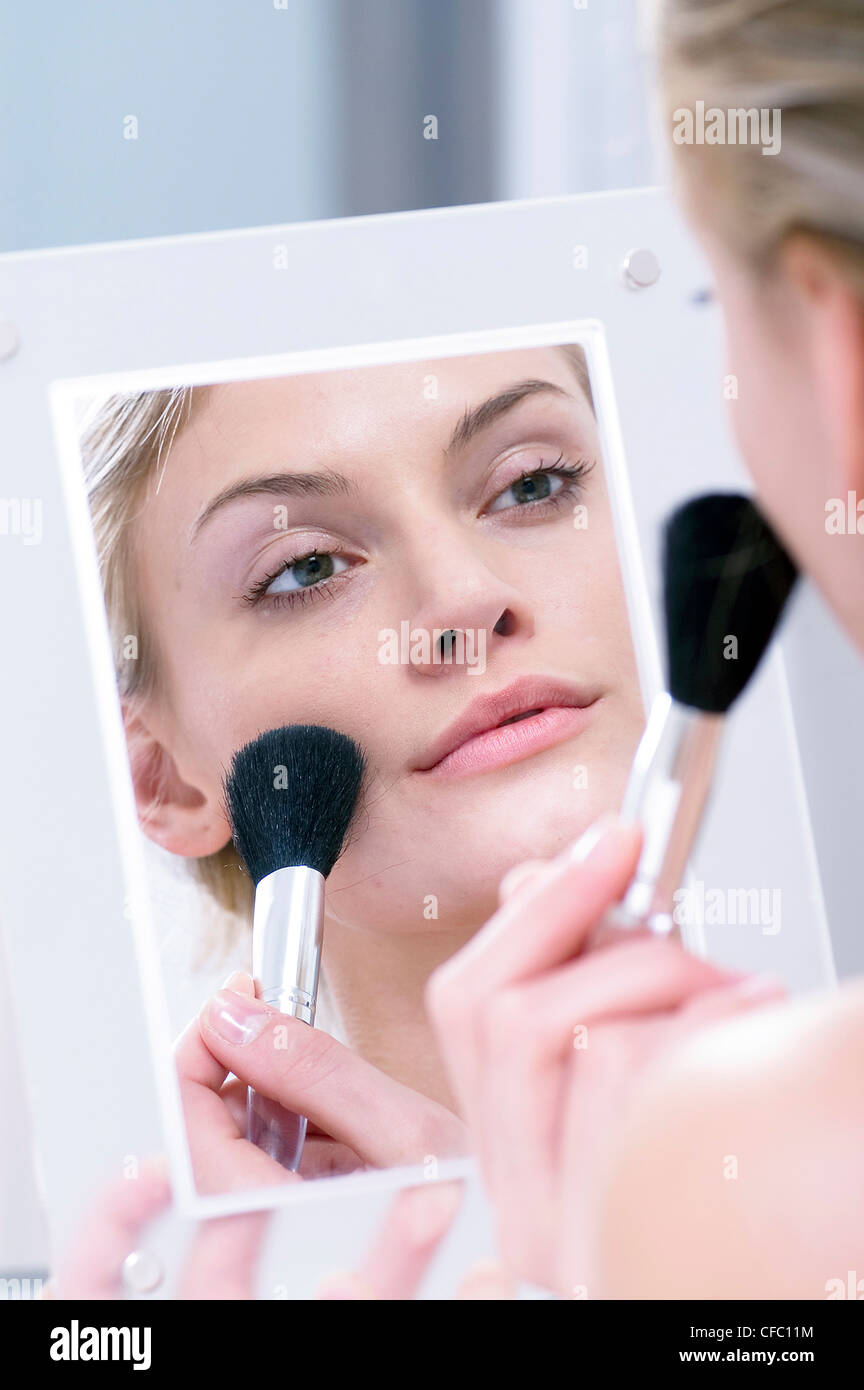 Femmina guardando il suo riflesso in uno specchio, applicando blusher alle sue guance con un pennello blusher Foto Stock