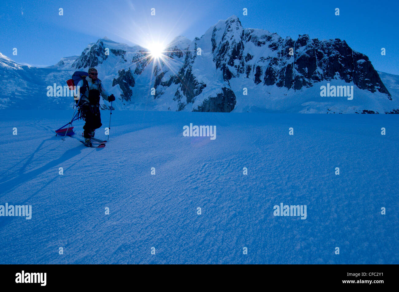 Uno sciatore traina un toboggan attraverso un ghiacciaio in remoto con un raggio di sole prenderci dietro ad alti picchi, gamma di Darwin, Cile Foto Stock